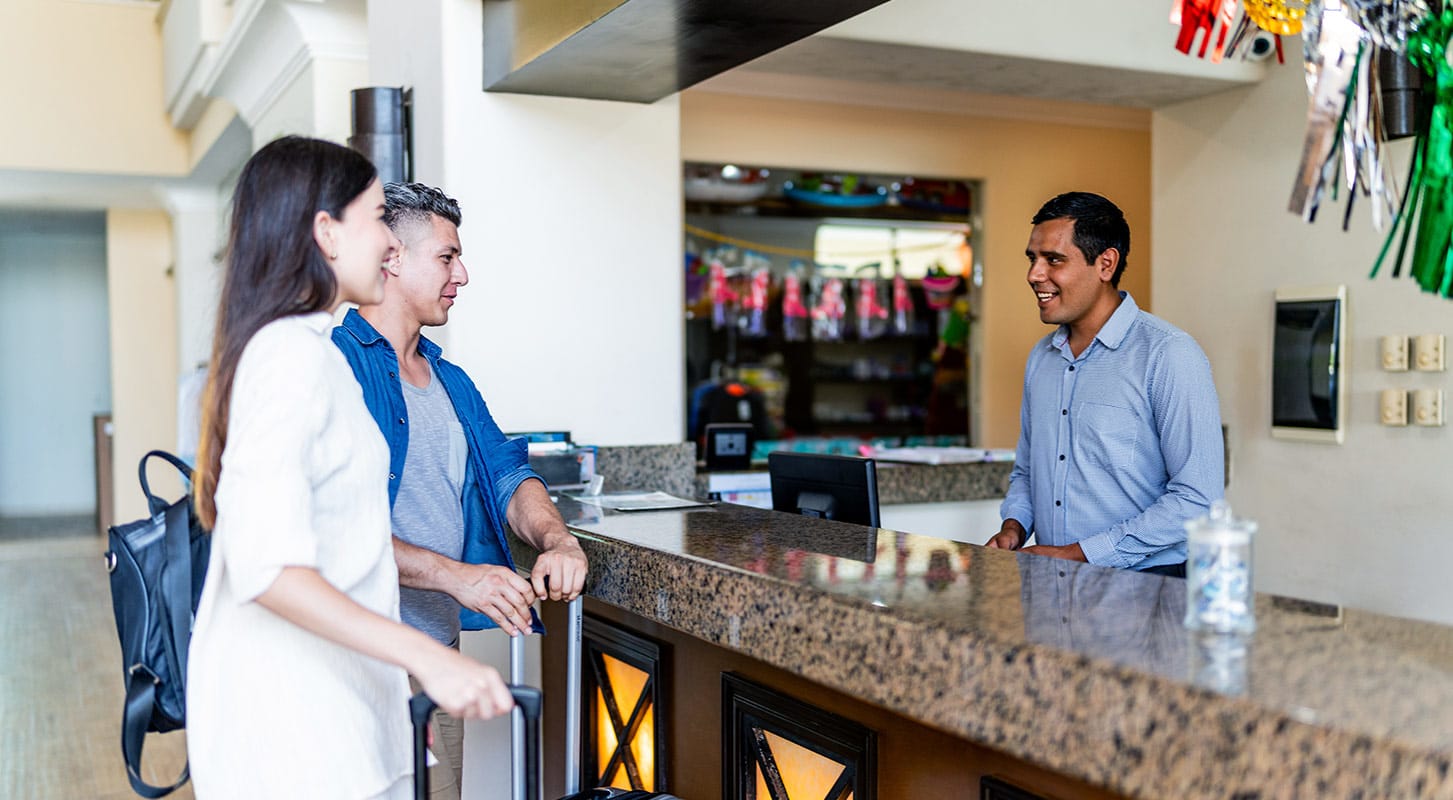 A couple stands at the hotel front desk, interacting with staff during check-in.
